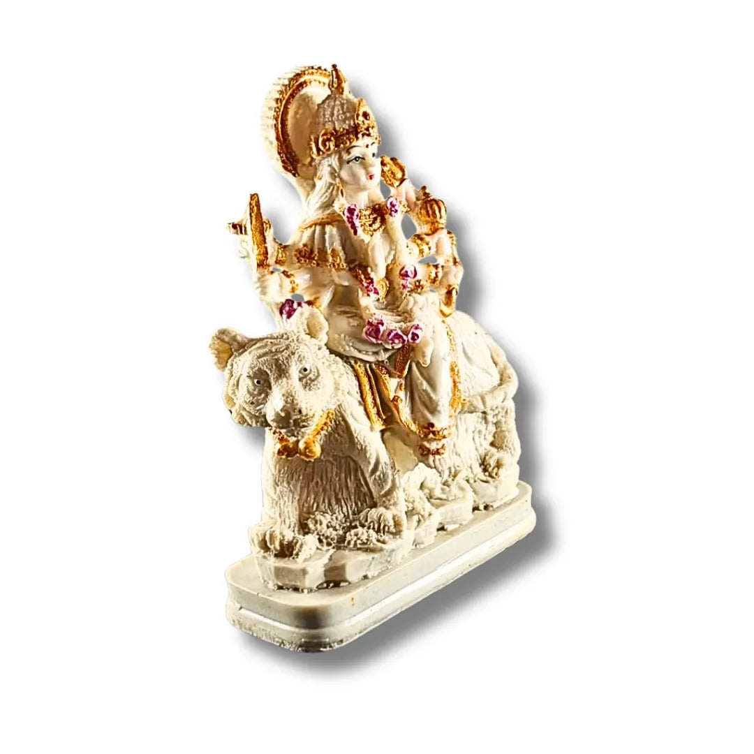 A small decorative statue of a Hindu deity riding a tiger, shown on a plain white background. The figure is primarily off-white/cream with prominent gold detailing and small pink floral accents.