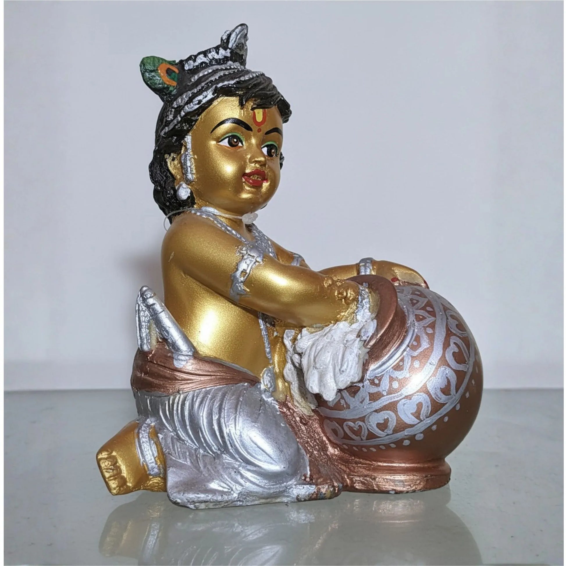 Decorative figurine of a seated figure with gold, silver, and brown colors on a white background