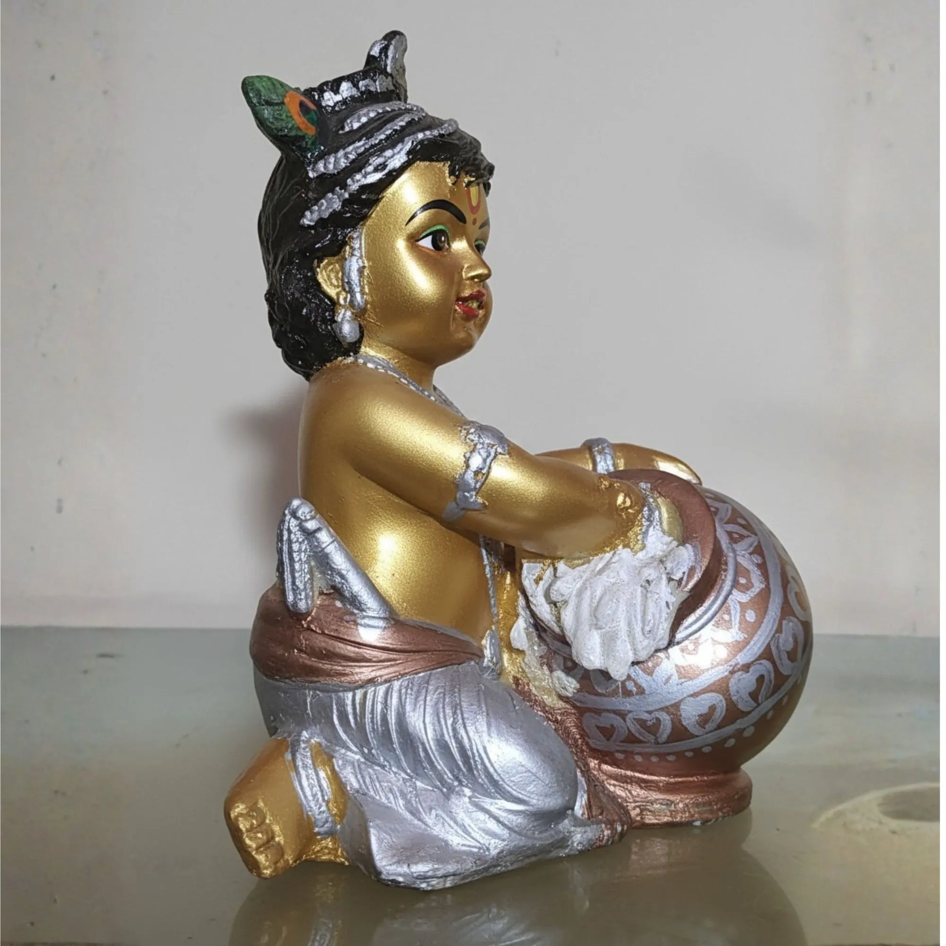 Decorative statue of a seated figure with gold, silver, and bronze colors on a plain background.