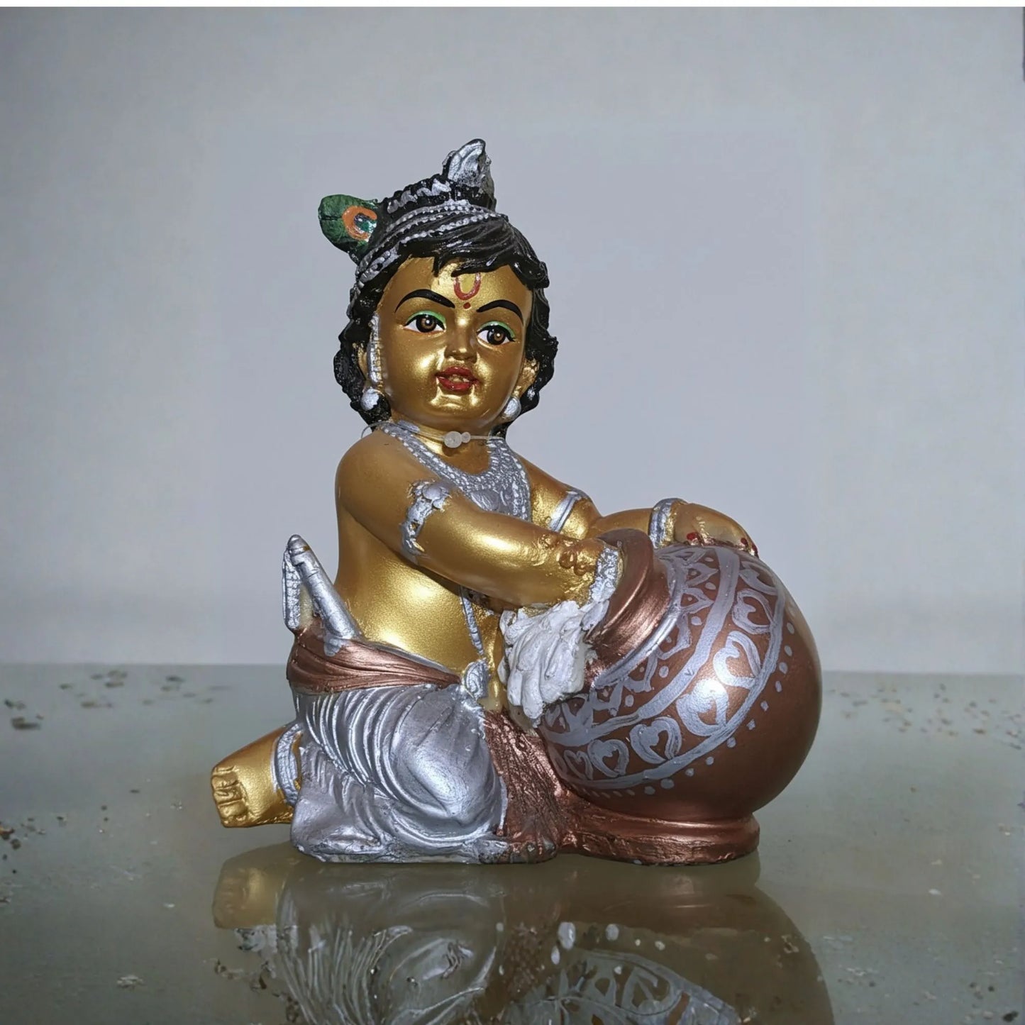 Decorative statue of a seated figure with gold, silver, and bronze colors on a reflective surface.