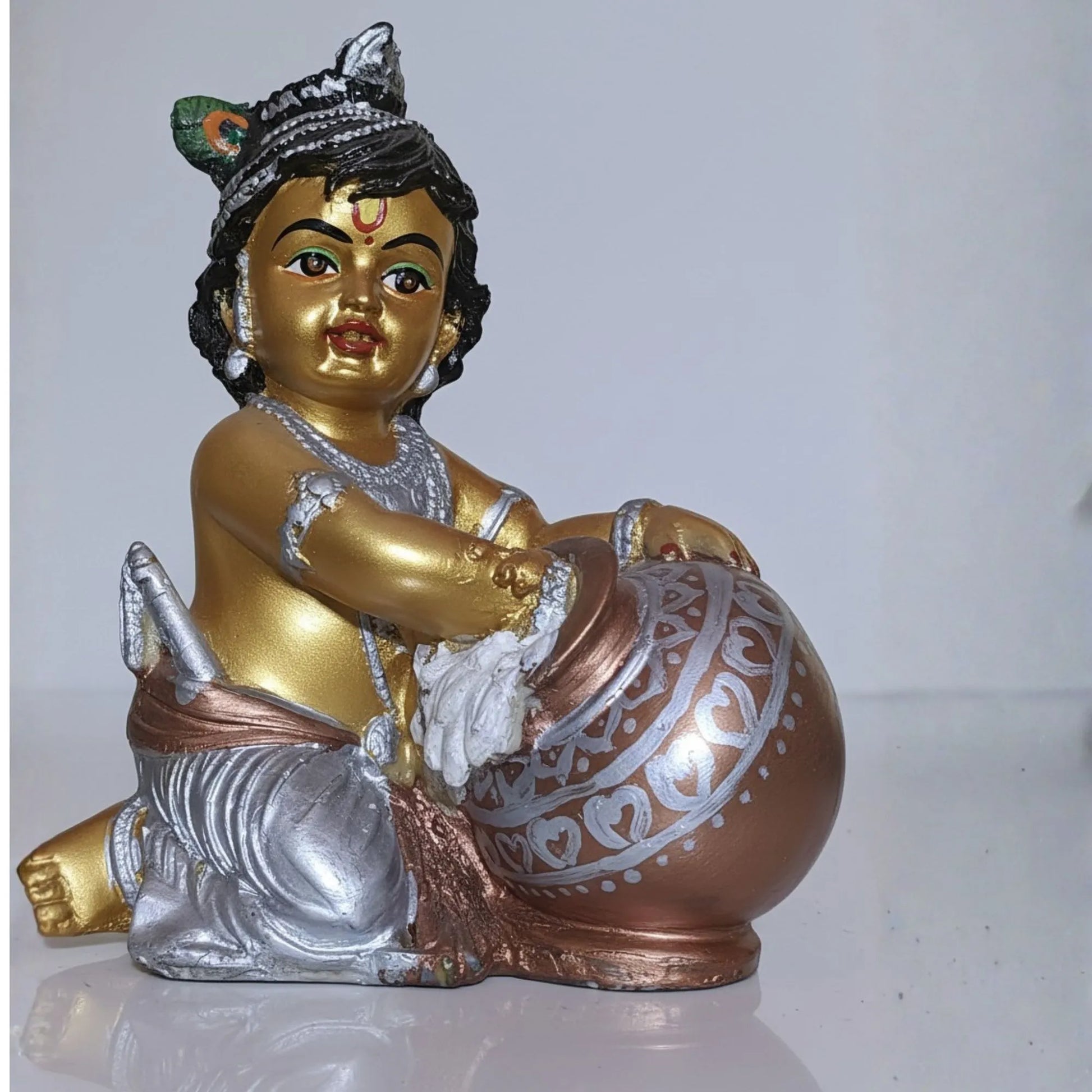 Statue of a child holding a drum with gold, silver, and bronze colors on a white background