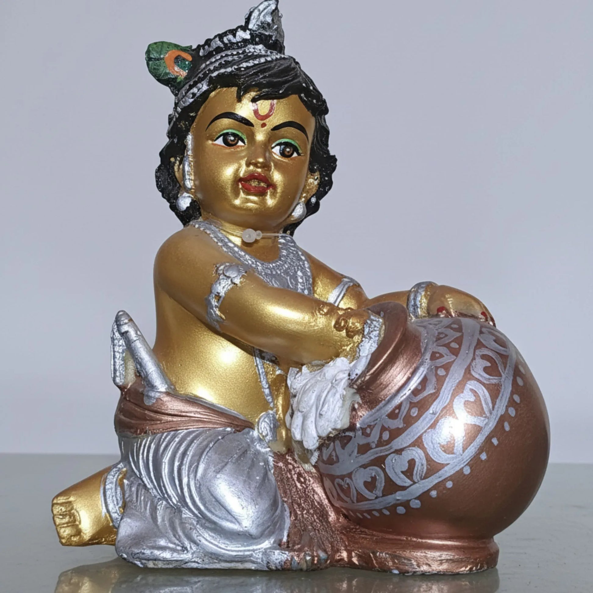 Statue of a child holding a pot with gold, silver, and bronze colors on a white background