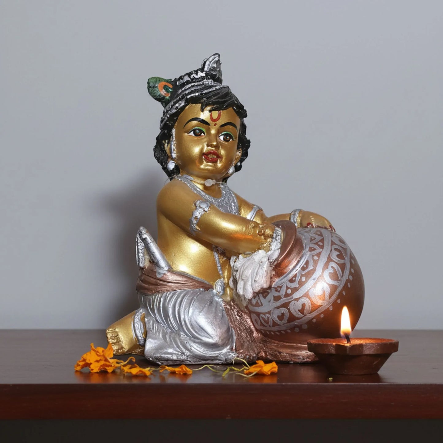 Decorative statue of a seated figure with gold and silver details on a wooden surface.