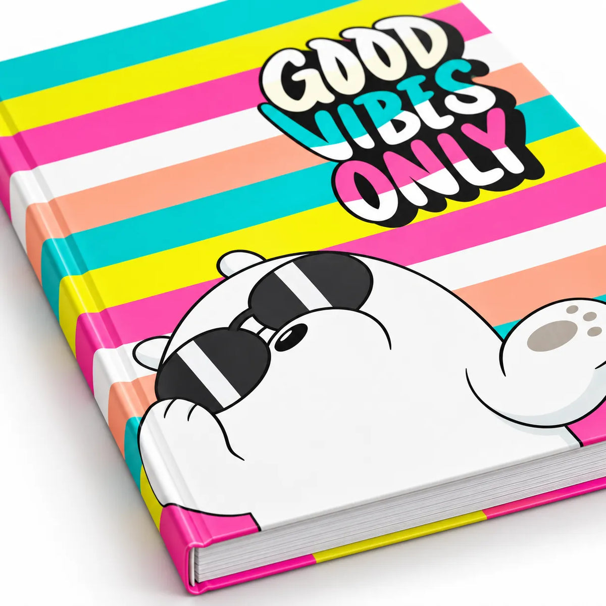 A hardcover notebook with a colorful striped cover featuring pink, yellow, teal, peach, and white horizontal bands. A cartoon white bear wearing black sunglasses peeks out from the bottom right, next to the text 'GOOD VIBES ONLY' in bold multicolor lettering.