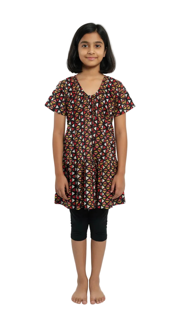 Young girl wearing a patterned dress and black capri pants on a white background