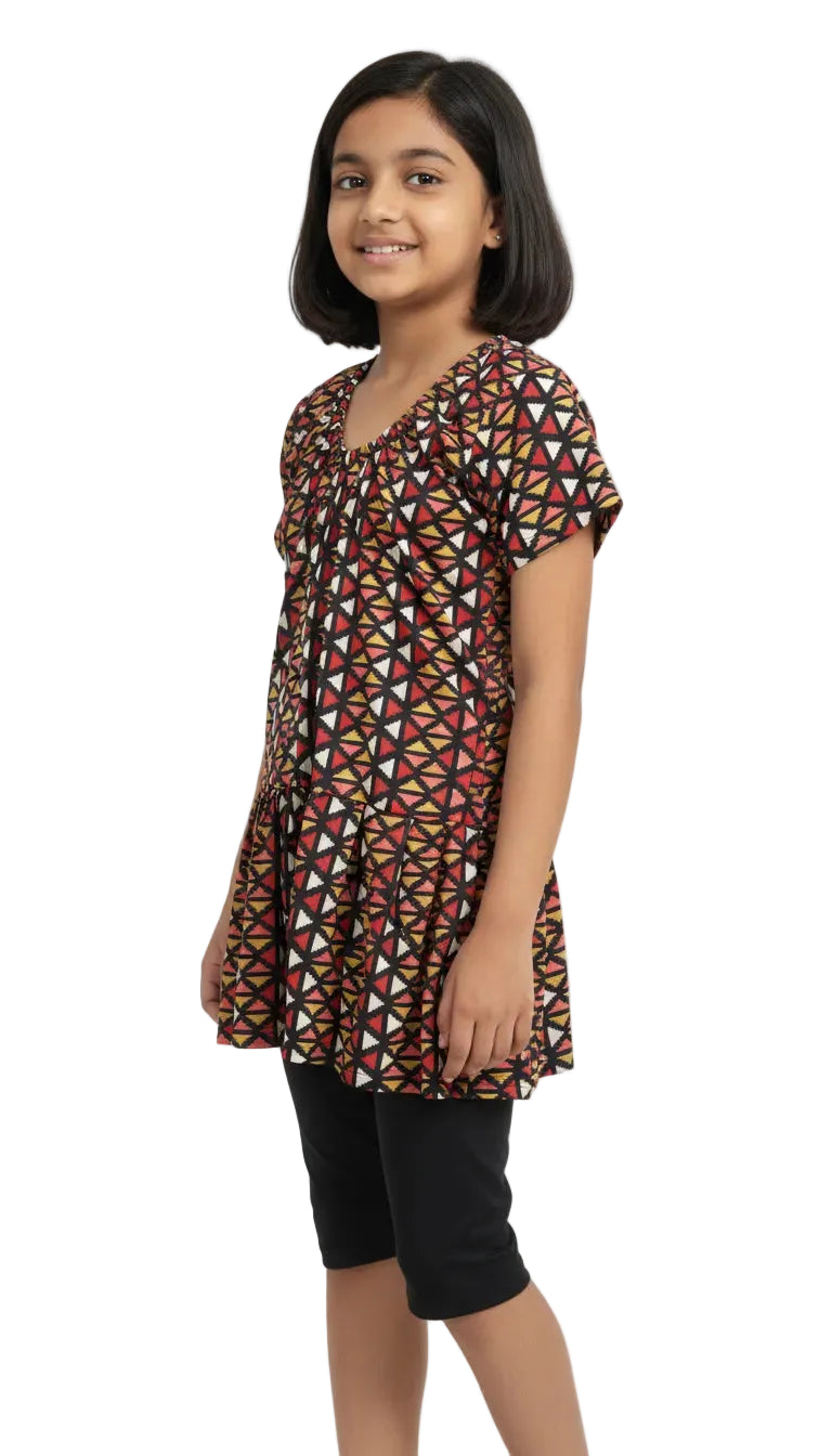 Young girl wearing a patterned top and black shorts on a white background