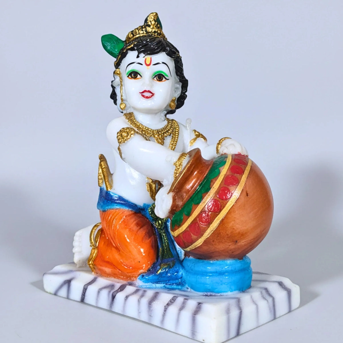 A colorful figurine of a child playing a large pot, seated on a striped base against a plain light gray background.