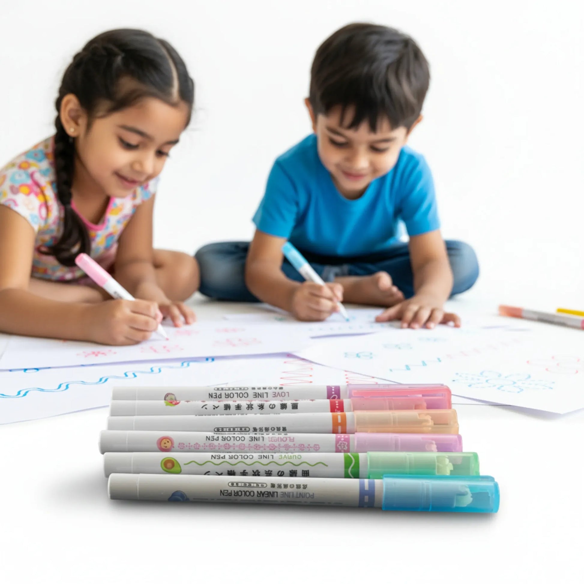 Two children sitting on the floor with markers and paper, surrounded by markers on a white background