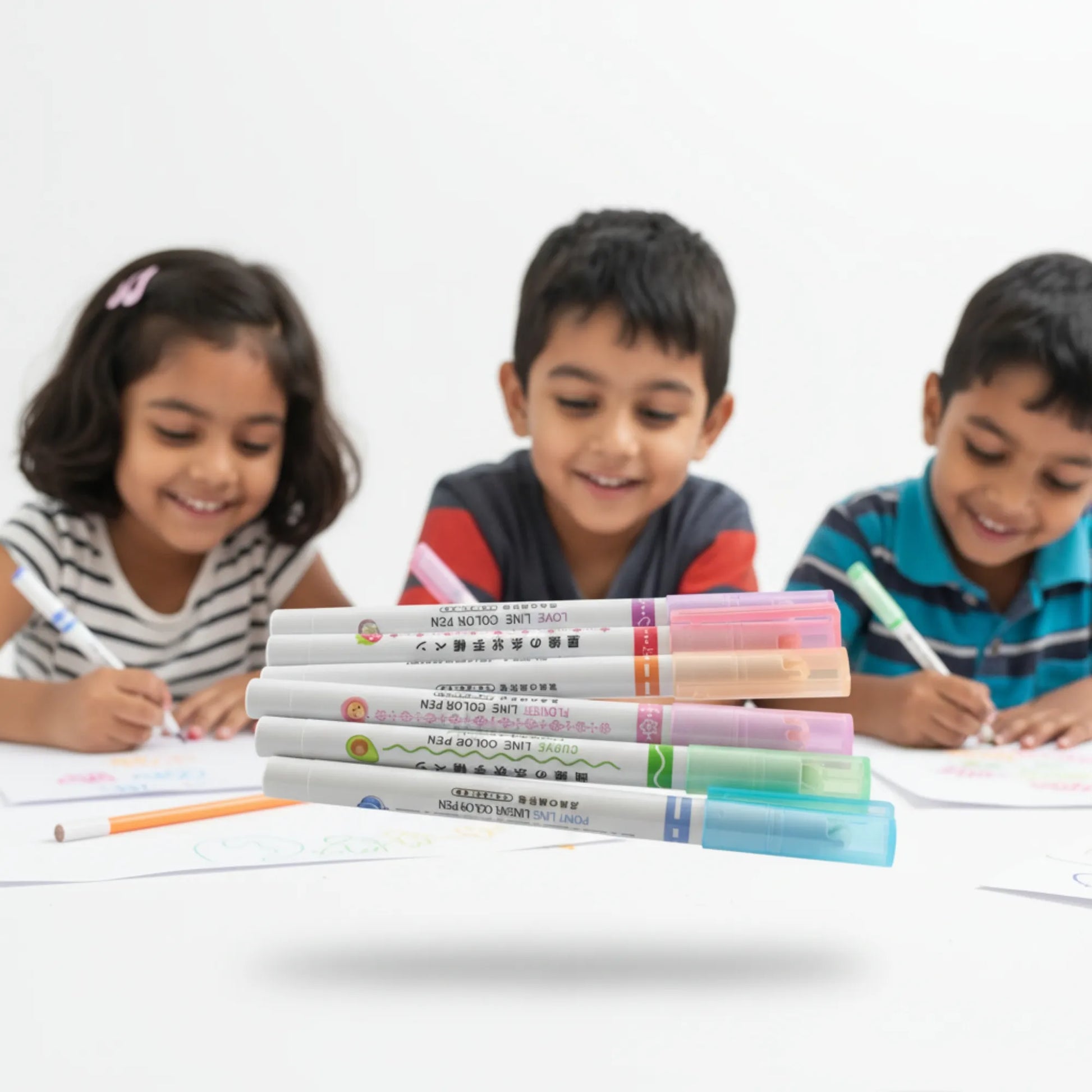 Three children sitting at a table with markers and books, smiling.