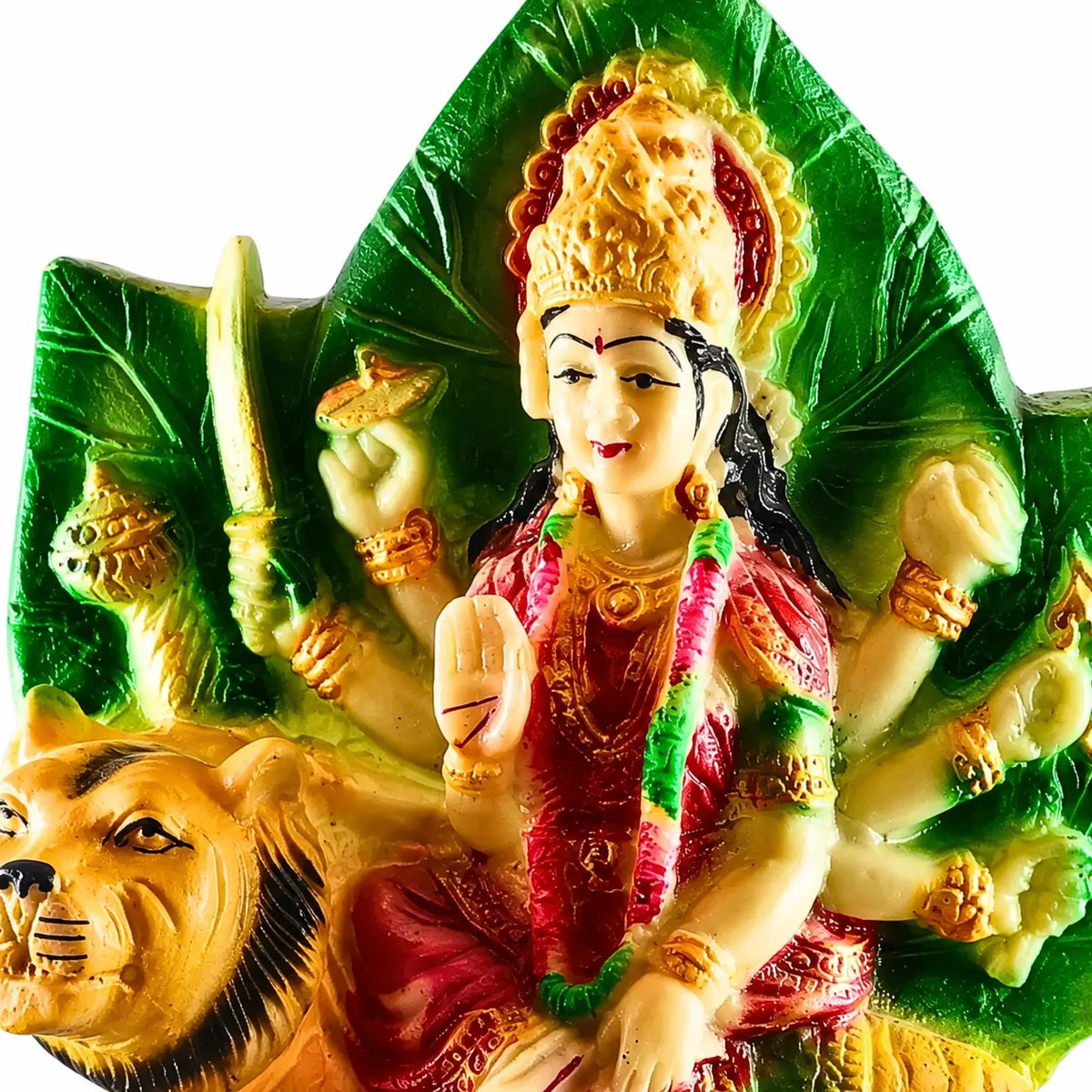 A colorful religious figurine of a multi-armed goddess seated on a lion, decorated with a gold crown and red garments, set against a green leaf-shaped backdrop on a white background.