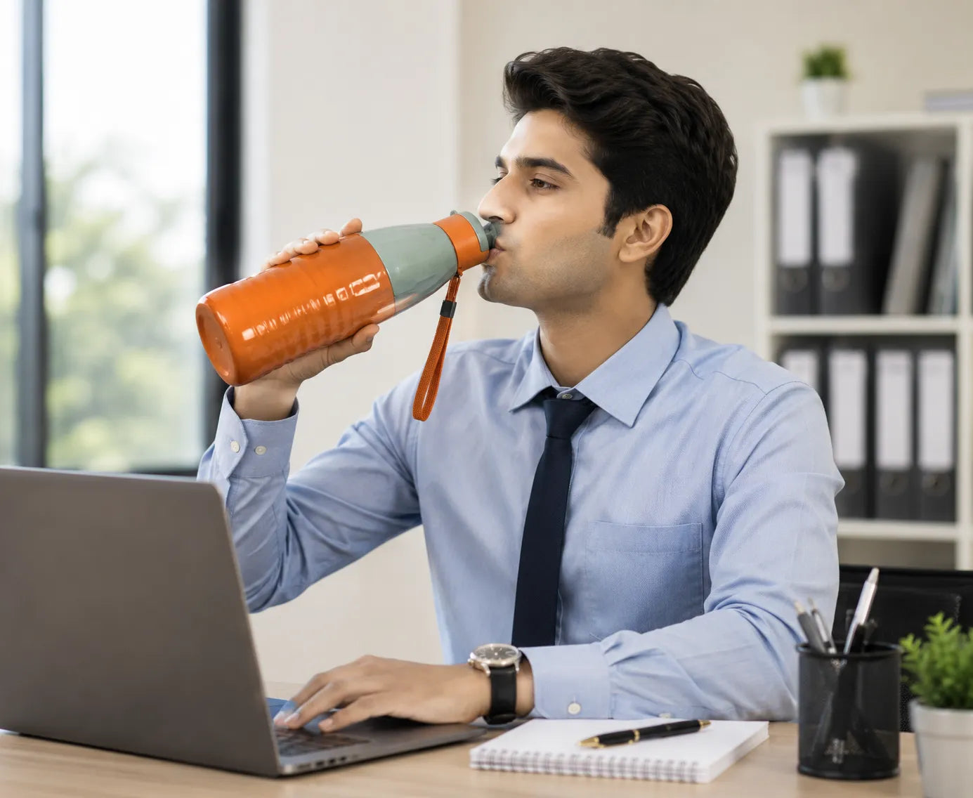 Man in a professional setting drinking from an orange water bottle.