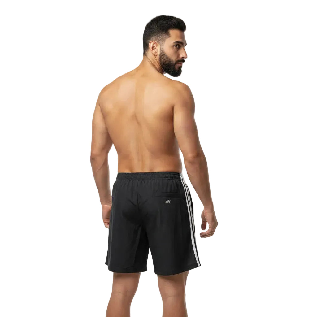 Man wearing black athletic shorts with white stripes on a plain background