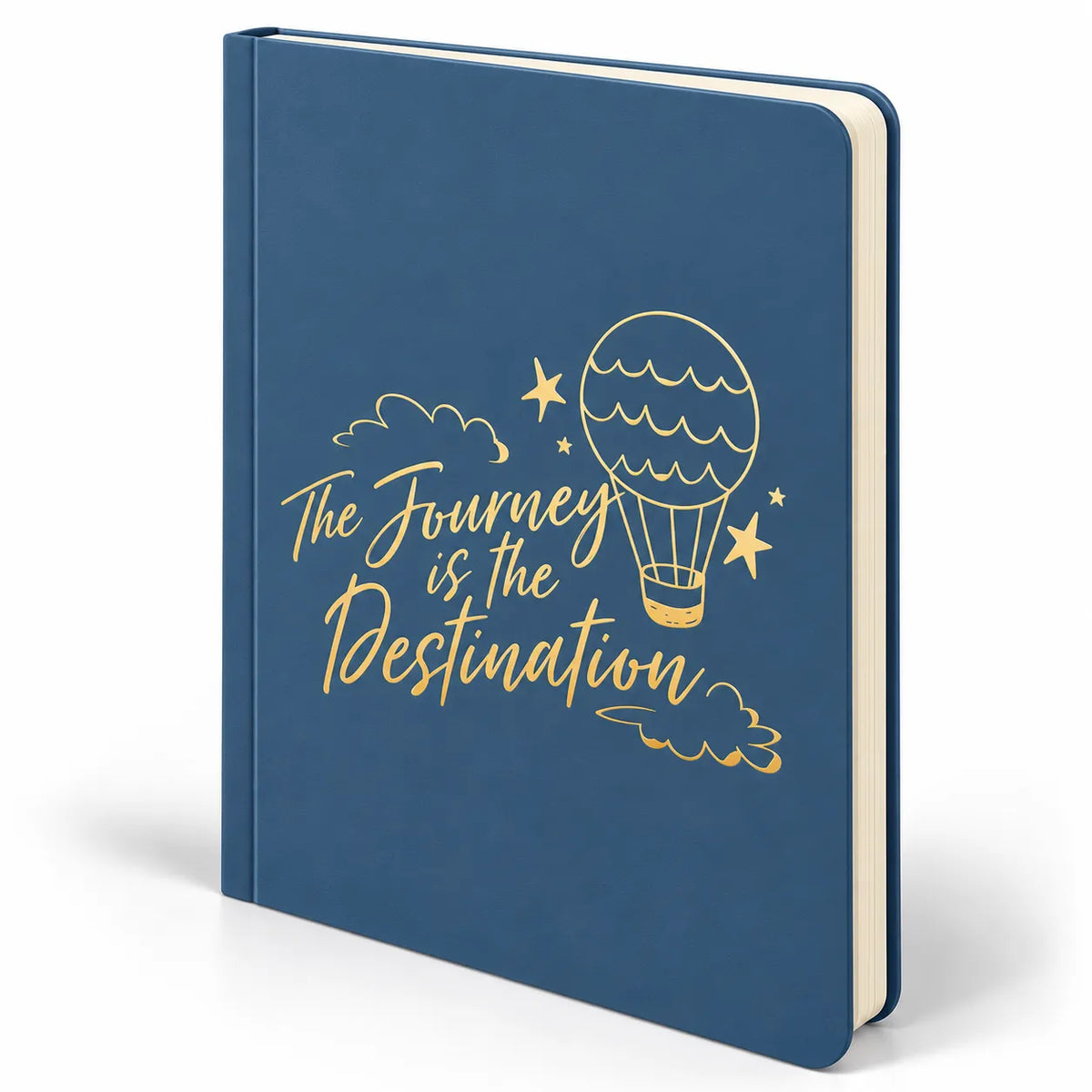 A hardcover notebook with a dark blue cover featuring a gold foil hot air balloon, stars, clouds, and the quote 'The Journey is the Destination' in gold script. The notebook is shown standing upright at a slight angle against a clean white background.