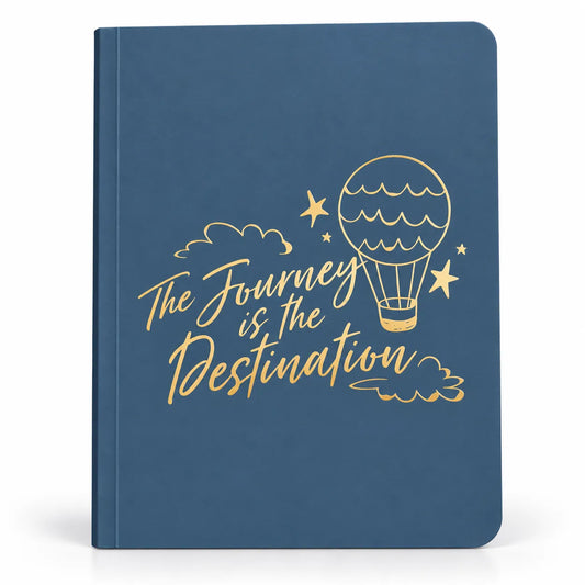 A blue hardcover notebook with gold foil lettering that reads 'The Journey is the Destination' and a gold hot air balloon illustration on the cover, shown against a plain white background.