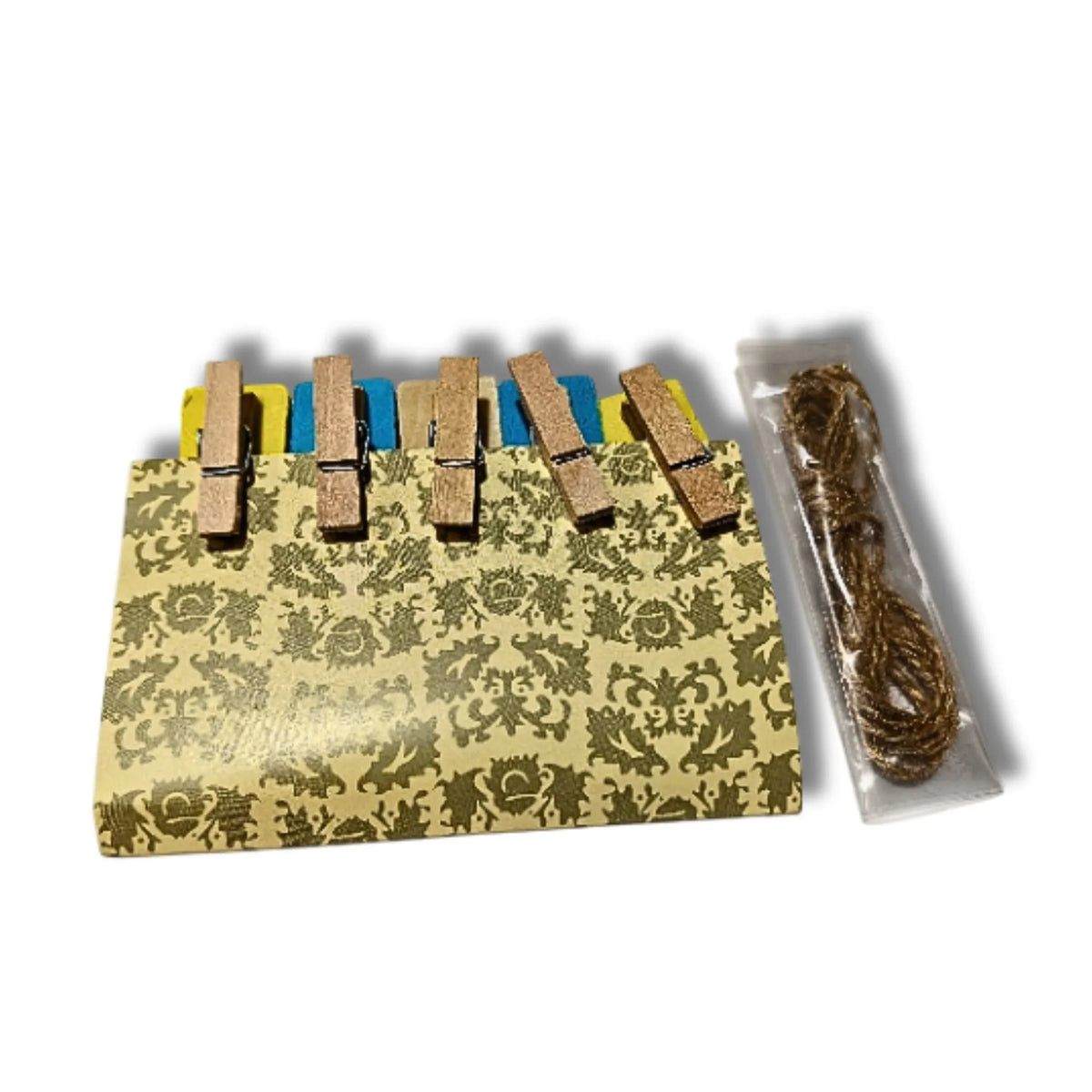 A set of five wooden clothespins with a decorative gold and beige damask patterned cover, shown alongside a clear plastic bag containing a brown twine bundle, on a white background.