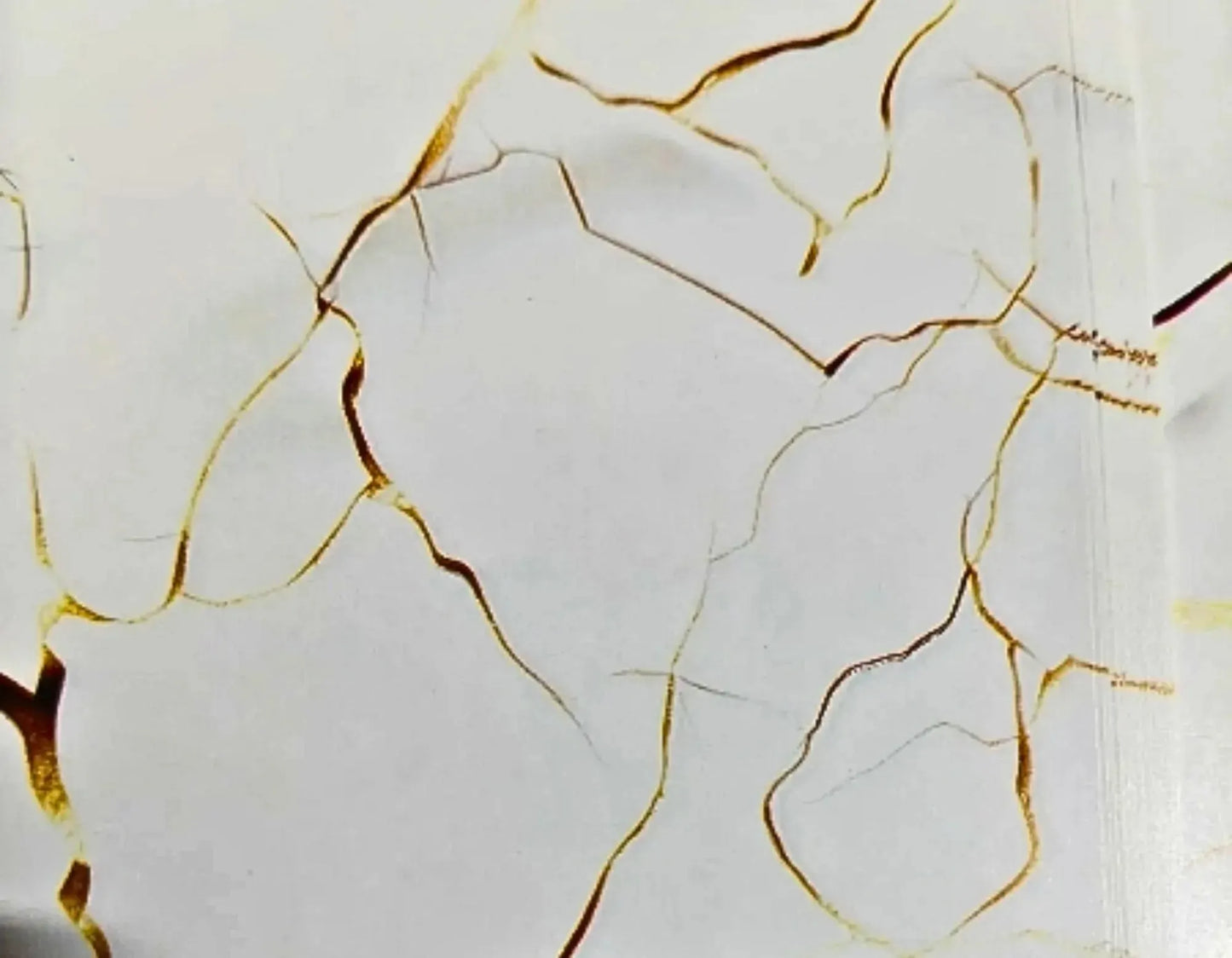 White marble-look surface with irregular metallic gold veining and a few darker brownish-gold marks.