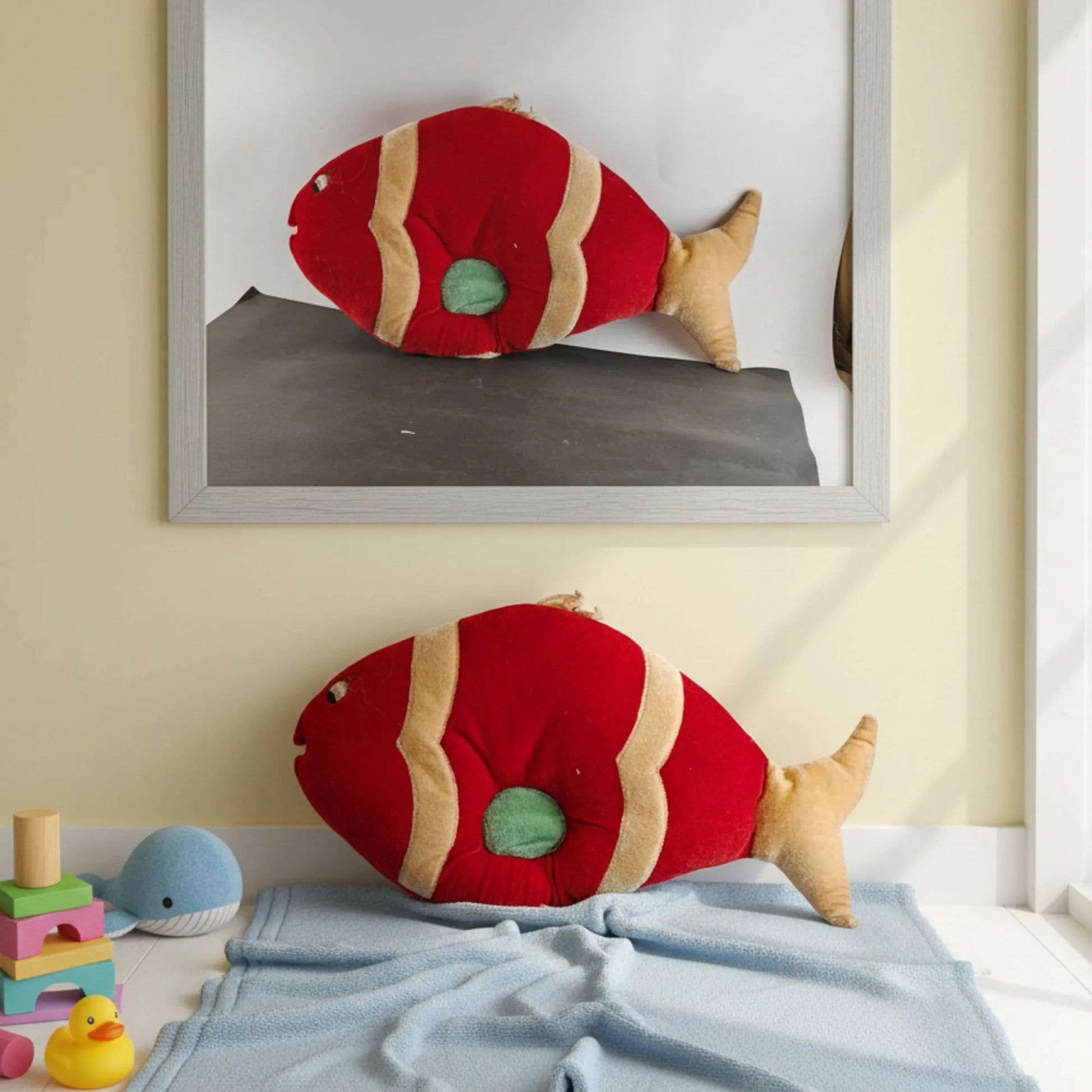 Red fish-shaped cushions on a bed with toys and a framed picture in the background.