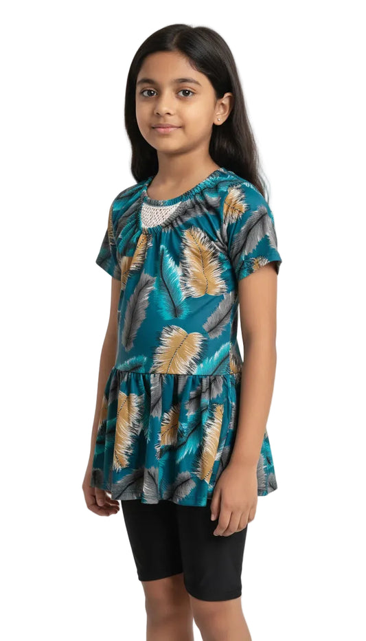 Young girl wearing a teal patterned top and black shorts on a white background